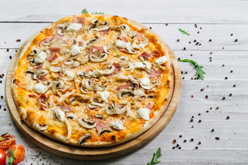 Tasty pizza with mozzarella, hum, chicken fillet, and champingnons on the white wooden background