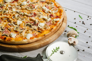 Tasty pizza with mozzarella, hum, chicken fillet, and champingnons on the white wooden background