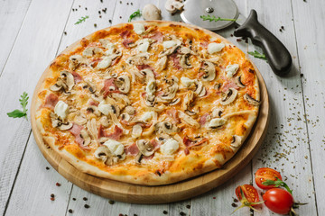 Tasty pizza with mozzarella, hum, chicken fillet, and champingnons on the white wooden background