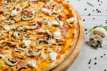 Tasty pizza with mozzarella, hum, chicken fillet, and champingnons on the white wooden background