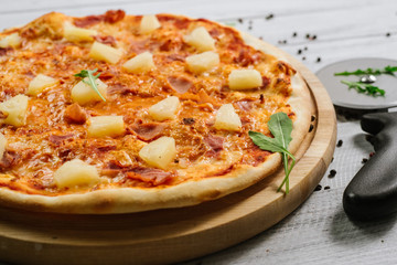 Tasty Hawaiian pizza with tomato sauce and pineapple on the white wooden background