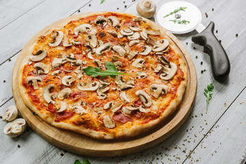 Tasty pizza Caprizzioza with tomato sauce, ham and champignons on the white wooden background
