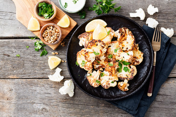 Black plate with tasty grilled cauliflower on wooden table.