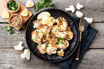 Black plate with tasty grilled cauliflower on wooden table.