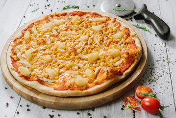 Pizza Americana with mozzarella, chicken fillet, pineapple and corn on the wooden background