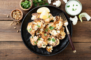 Black plate with tasty grilled cauliflower on wooden table.