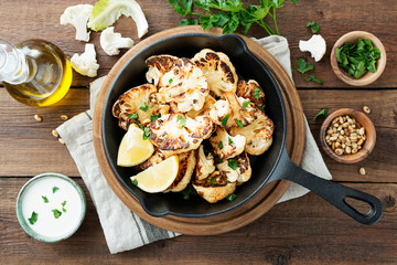 Black plate with tasty grilled cauliflower on wooden table.