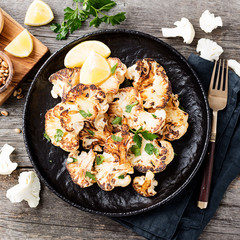Black plate with tasty grilled cauliflower on wooden table.