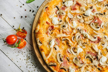 Tasty pizza with mozzarella, hum, chicken fillet, and champingnons on the white wooden background