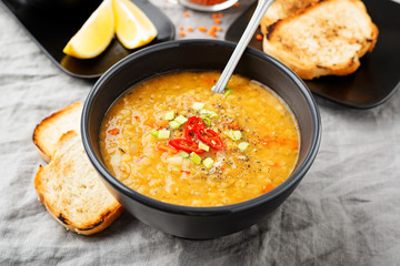 Lentil soup with  bread in a dark ceramic  bowl on a gray textile background .