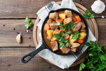 Meat stewed with potatoes, carrots and spices in iron pan on wooden background .