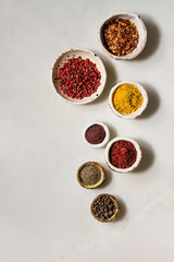 Spices seasoning and herbs variety in ceramic bowls. Different ground peppers, chili pepper, turmeric, bay leaf, cinnamon over white marble background. Flat lay, space. Cooking concept