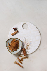 Spices cinnamon powder and sticks, anise star in ceramic plate on ceramic board over white marble background. Flat lay, space. Cooking concept