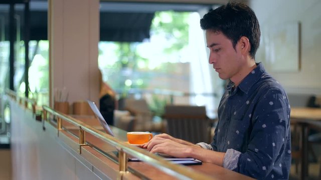 Attractive hispanic man sitting in coffee shop typing on laptop and drinking coffee, medium shot