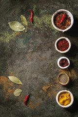 Spices seasoning and herbs variety in ceramic bowls in row. Different ground peppers, chili pepper, turmeric, bay leaf, cinnamon over dark metal background. Flat lay, space. Cooking concept