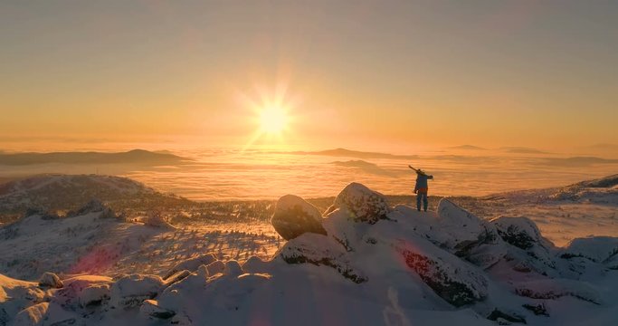 skier on top of the mountain, skiing on his shoulder and salutes the victory. sunrise, sunset. mountain valley. above the clouds. rear view. aerial view. stock video footage. back light. camera move