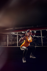 Close up of a young strong fitness female model doing squats with weight.