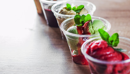 various ice cream desserts a plastic cups with mint leaf on wooden table