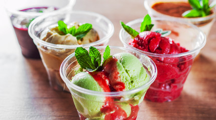 various ice cream desserts a plastic cups with mint leaf on wooden table