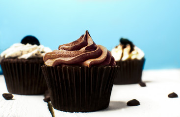 A closeup of delicious cupcakes with chocolate and vanilla frosting on a sky blue background and white wooden stand. Poster for birthday celebration or coffee shop, bakery advert concept. 