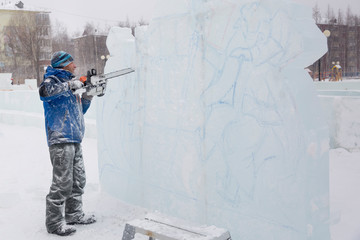 The sculptor cuts a figure from an ice block with a gasoline saw