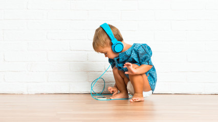Adorable little baby listening music on white brick background