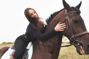 Young cute girl hugging her horse while sitting astride. She likes animals
