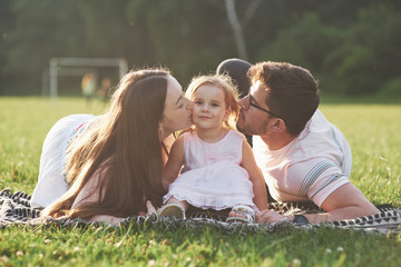 Fototapeta premium Mother and father spend time together happily. Little daughter plays with her parents outdoors during sunset