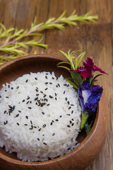 Wooden plate with jasmine rice and black sesame seeds on a wooden background