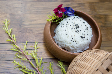 Wooden plate with jasmine rice and black sesame seeds on a wooden background