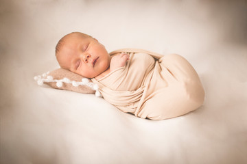 Newborn baby in a winding on a beige background