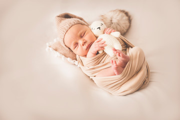 Fototapeta na wymiar Newborn sleeping boy with a toy on a beige background