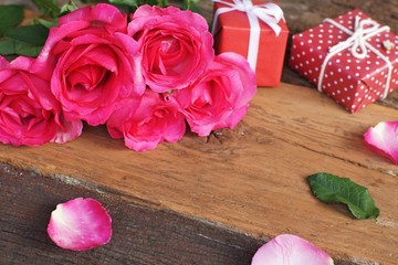 Obraz na płótnie Canvas Elegant pink rose, gift box decorated with petals and card with natural soft light on wood background, beautiful valentine's day background concept