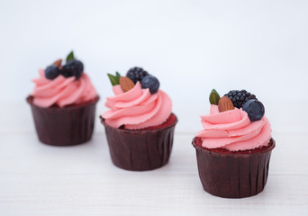 three cupcakes with pink cream, berries and almonds on white background