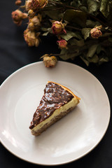 Top view of chocolate cheesecake and flowers on black background