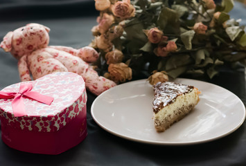 Chocolate cheesecake, rose teddy bear, flowers and gift box on black background