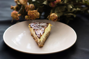 Slice of cheesecake with chocolate and flowers on black background