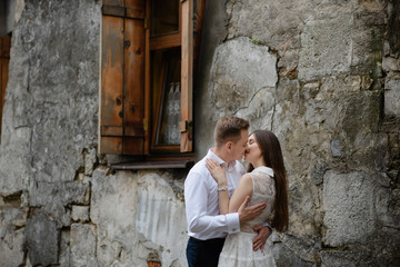 Obraz na płótnie Canvas Couple in love is kissing and hugging over the grey urban wall in the morning city. Man and woman are having great time together. Ancient old european city street with stone walls.