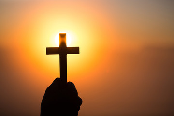 Silhouette of woman hands praying with cross  in nature sunrise background,  Crucifix, Symbol of...