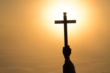 Silhouette off hands holding wooden cross  on sunrise background, Crucifix, Symbol of Faith.