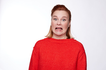 Terrified red haired woman yells and keeps eyes popped out, wears red oversized sweater, looses...