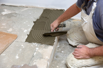 The construction worker evenly spreads the surface of the stairs with cement adhesive mass using a...