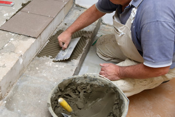 The construction worker evenly spreads the surface of the stairs with cement adhesive mass using a special hand tool.