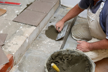 The construction worker evenly spreads the surface of the stairs with cement adhesive mass using a special hand tool.
