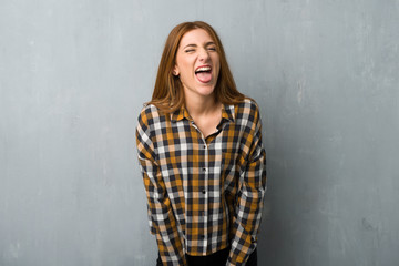 Young redhead girl over grunge wall showing tongue at the camera having funny look