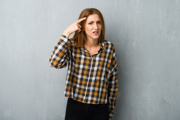 Young redhead girl over grunge wall making the gesture of madness putting finger on the head