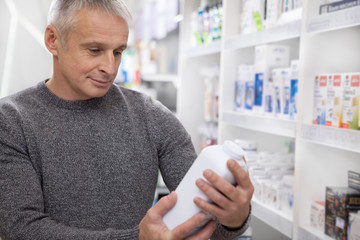 Cheerful senior man shopping at the drugstore, examining label of a medical product. Mature male customer buying goods at the pharmacy. Consumerism, health care, purchasing concept