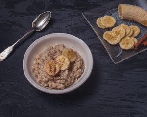 Oatmeal for breakfast with cinnamon and banana. Located on a wooden dark table.