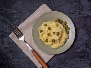 Mashed potatoes with canned peas on a light linen napkin and a dark wooden background.
