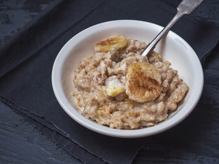 Deep ceramic plate with porridge, sprinkled with cinnamon and banana circles. There is a dark cotton napkin under the plate.